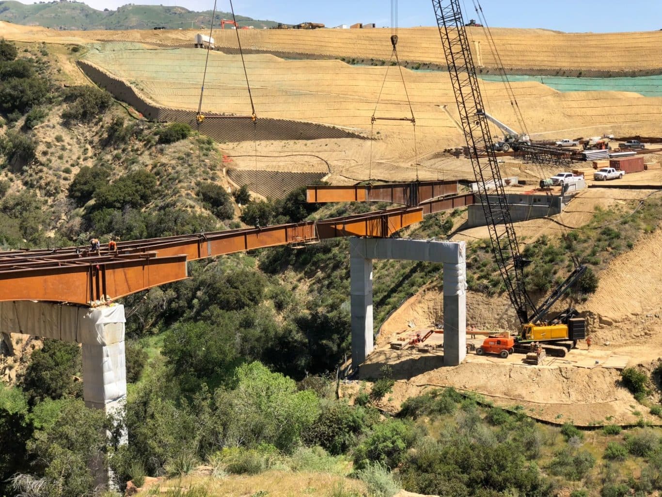 Steel bridge girders being placed across a canyon during land development construction