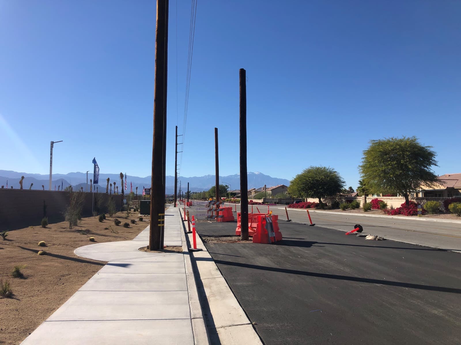 Fresh asphalt and a new sidewalk on a residential street, with wooden power poles along the shoulder