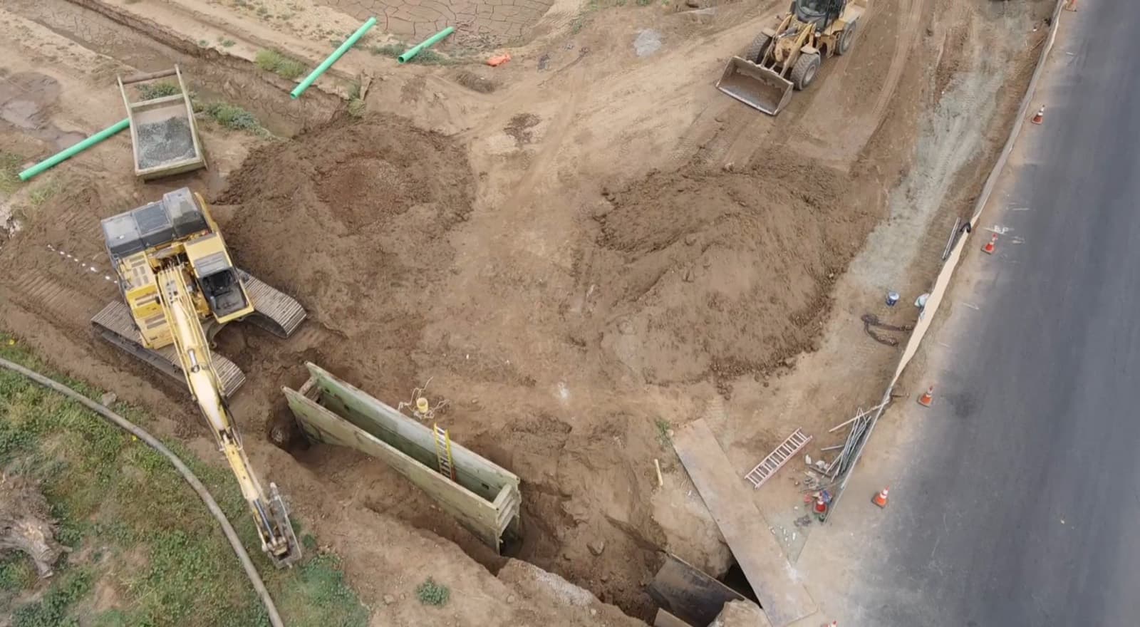 Workers inside a shored trench at a deep sewer tie-in, with a crane truck at the surface
