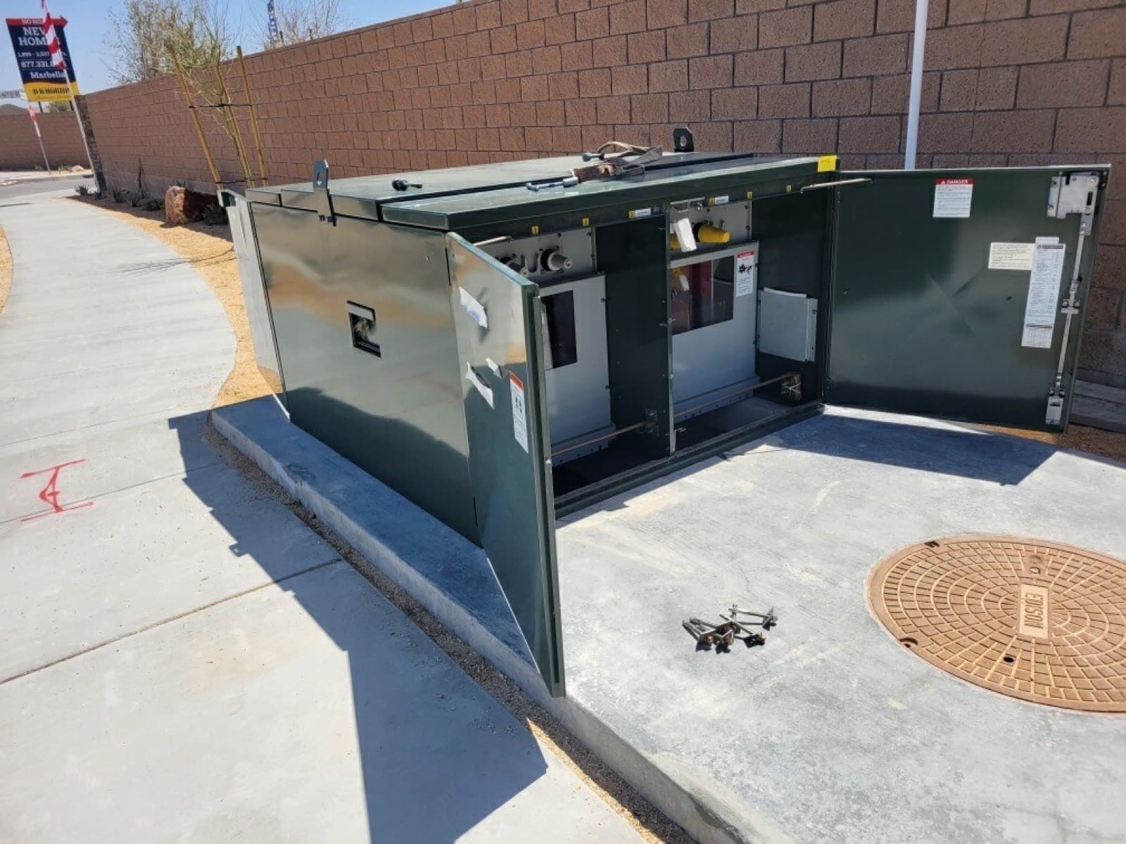 An open electrical cabinet on a new sidewalk, with conduit and wires inside